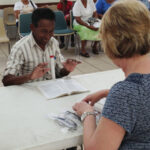 A patient is excited to be able to see and expresses his delight while a volunteer adjusts his new glasses