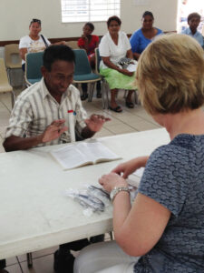 A patient is excited to be able to see and expresses his delight while a volunteer adjusts his new glasses